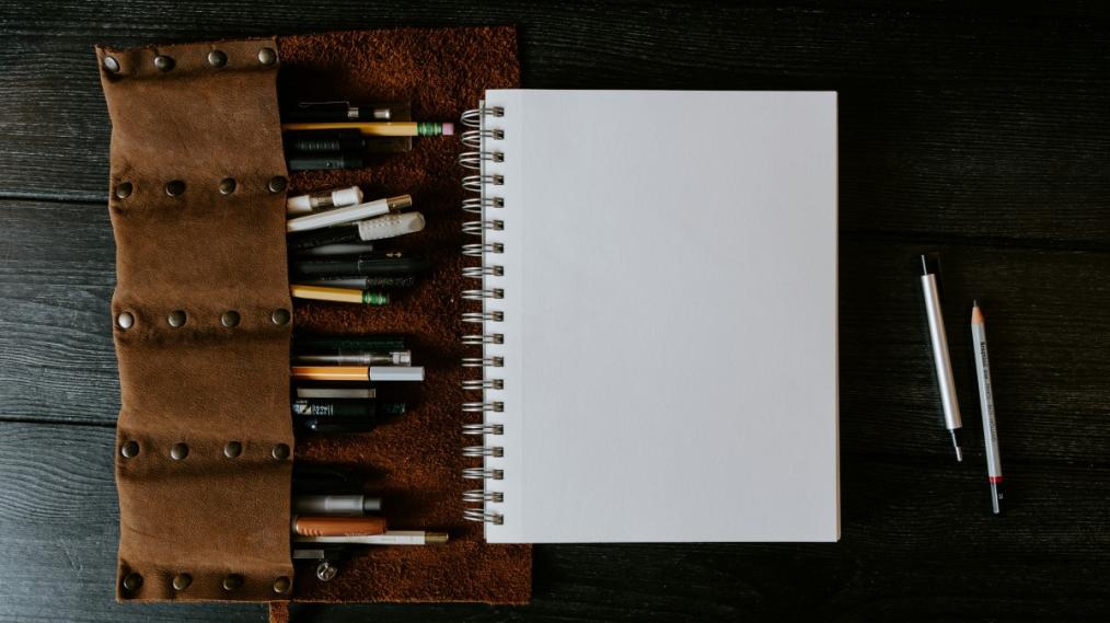 One notebook page with pencils and pens around it.