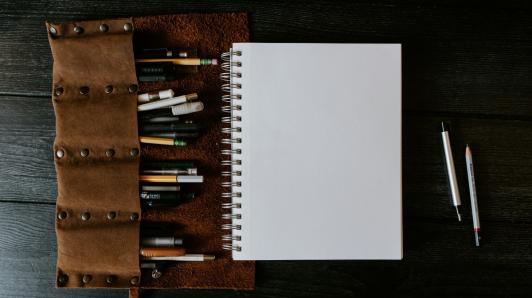 One notebook page with pencils and pens around it.