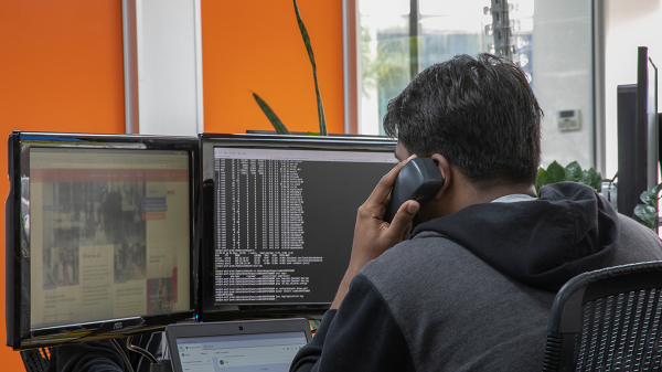 Man talking on the phone while looking at two desktop screens.
