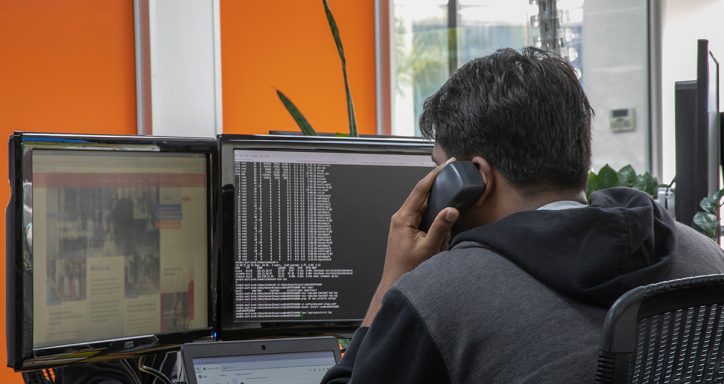Man talking on the phone while looking at two desktop screens.