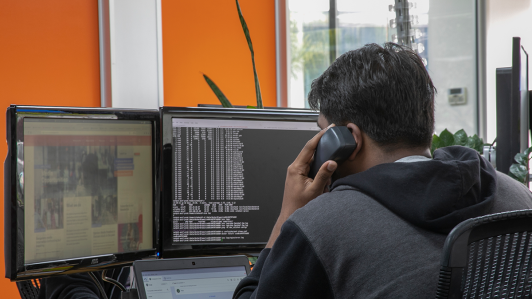 Man talking on the phone while looking at two desktop screens.